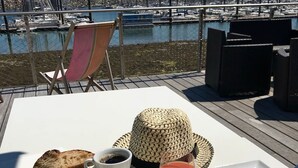 Een tafel gedekt met eten en drinken op een terras met uitzicht op een jachthaven.