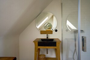 Een badkamer met een houten wastafelmeubel, een ronde spiegel en een douchehoek.