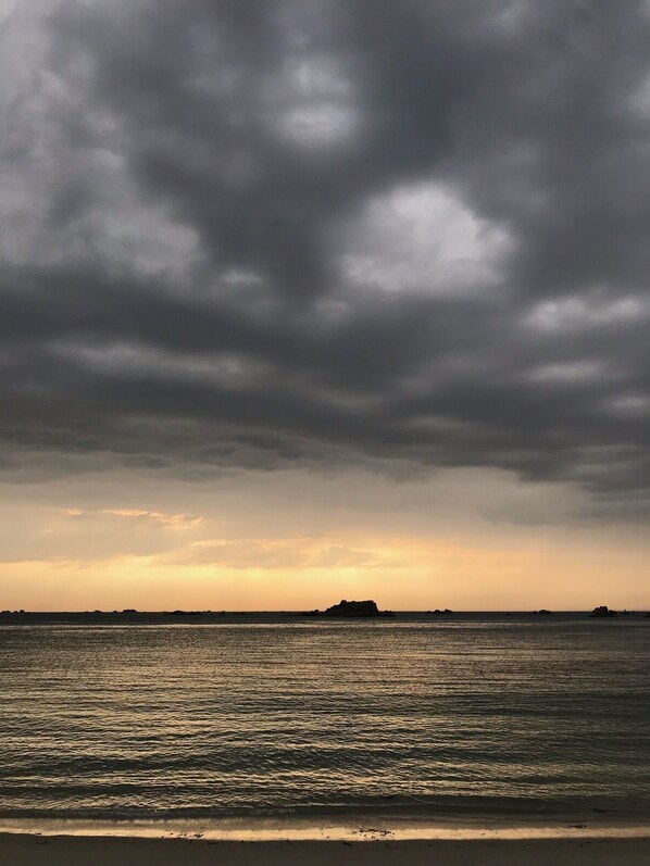 Paesaggio costiero con mare calmo, un'isola in lontananza e cielo nuvoloso.