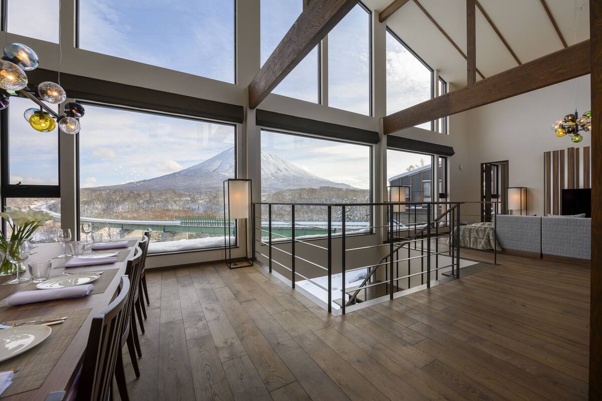 A spacious dining area with a view of a mountain, wooden floors, and a staircase leading to an upper level.