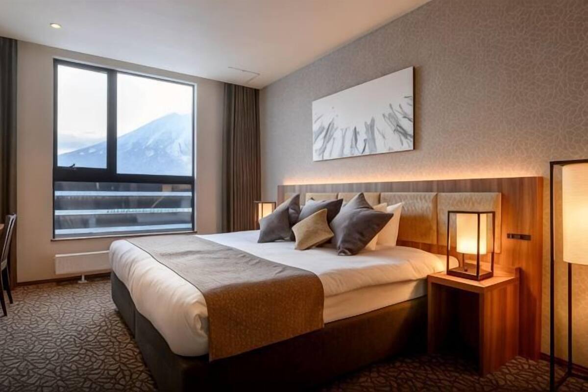 A hotel room with a large bed, a view of mountains through a window, and a painting on the wall.