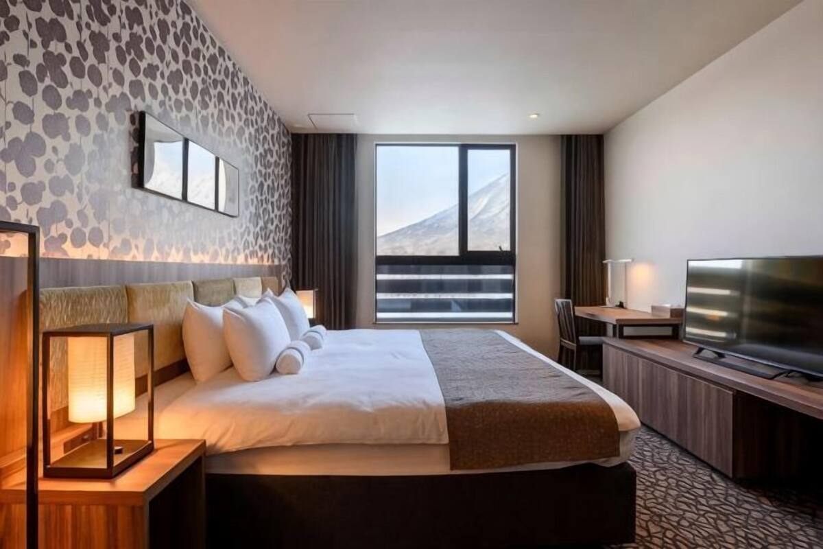 A hotel room with a large bed, a TV, a desk, and a view of a mountainous landscape.