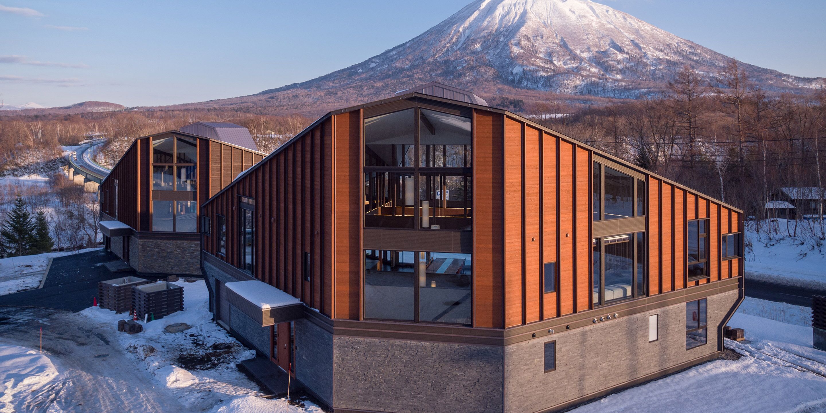 A modern building with large windows and a wooden facade, situated in a snowy landscape with a mountain in the background.