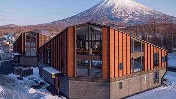 A modern building with large windows and a wooden facade, situated in a snowy landscape with a mountain in the background.