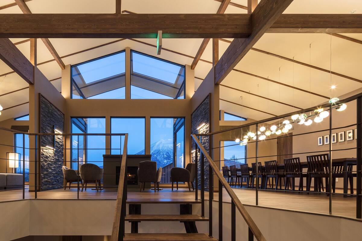 A spacious interior with a high ceiling, large windows, and a staircase leading to a dining area.