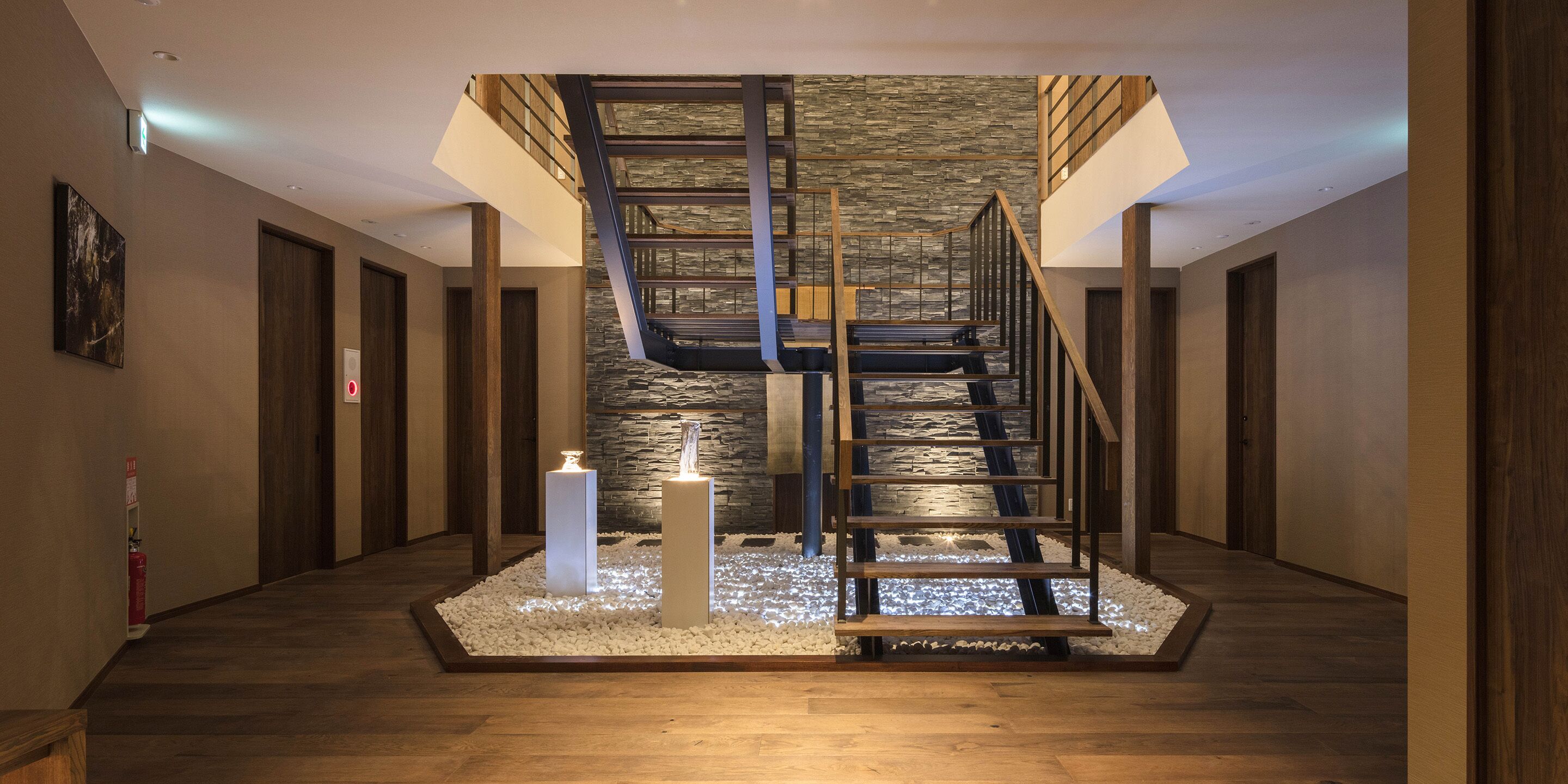 A modern staircase with a stone wall backdrop, wooden railings, and a minimalist design.