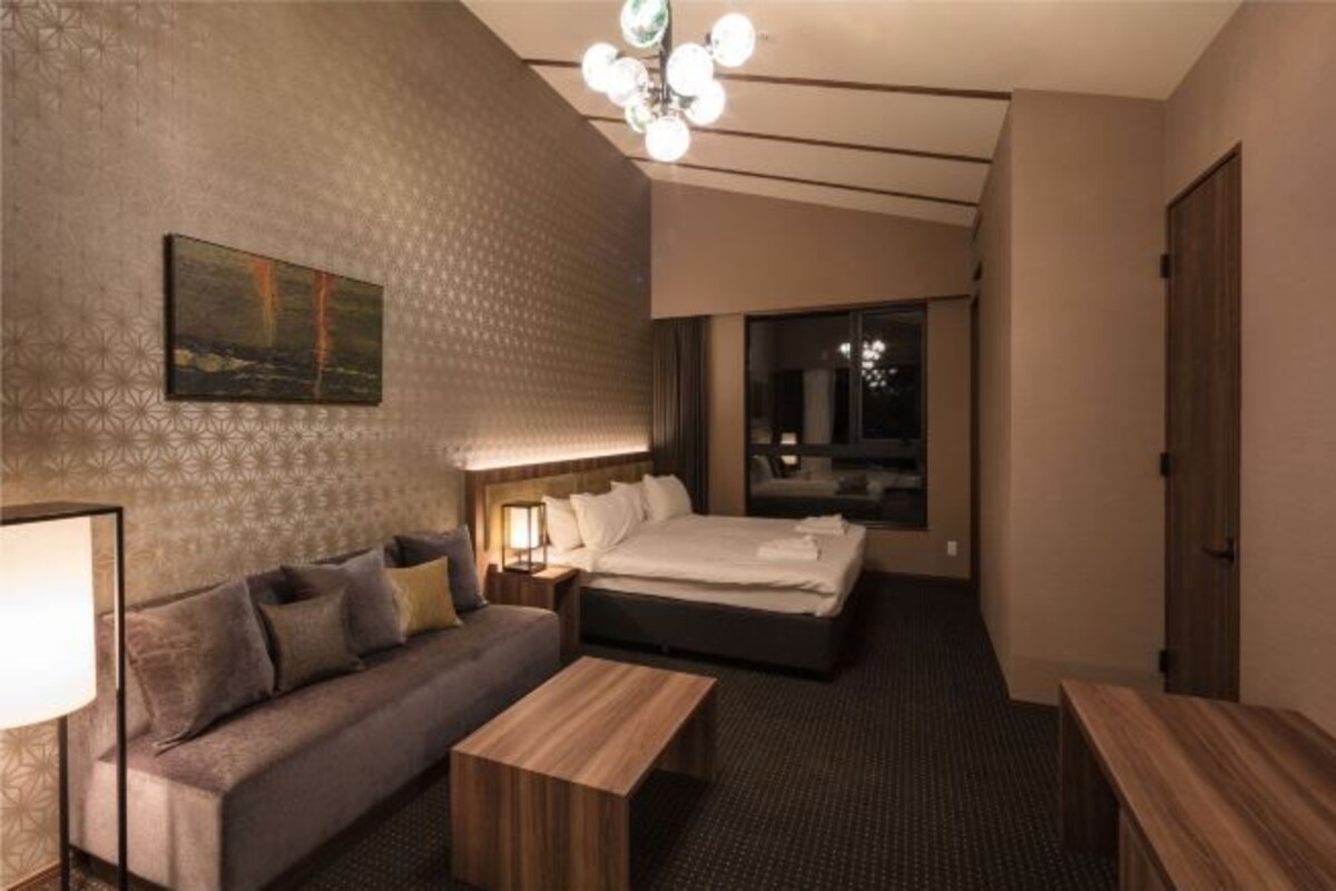 Un cuarto de hotel con una cama grande, un sofá, una mesa de centro de madera, un cuadro en la pared y una araña.