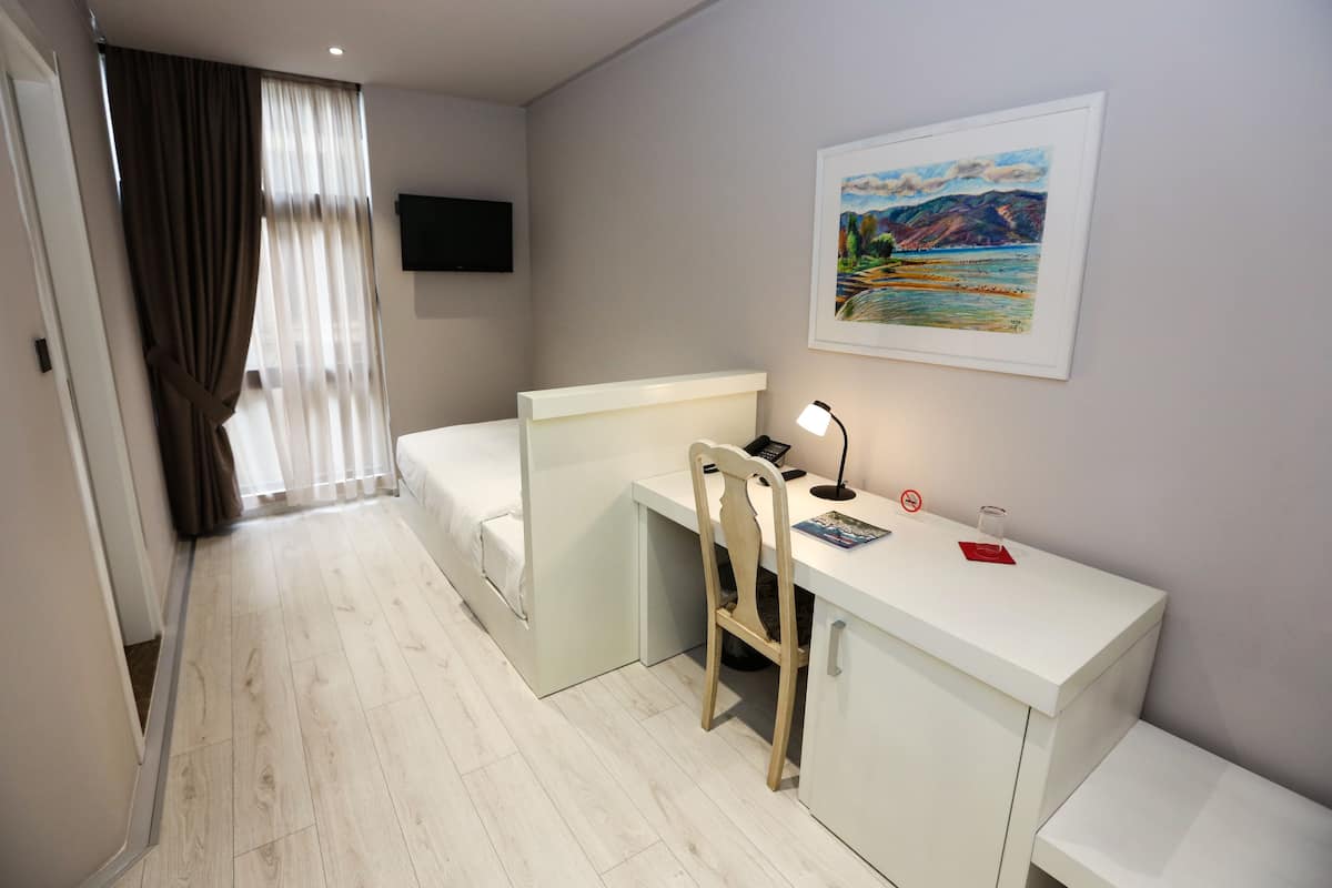 A hotel room with a desk, chair, and a painting on the wall.