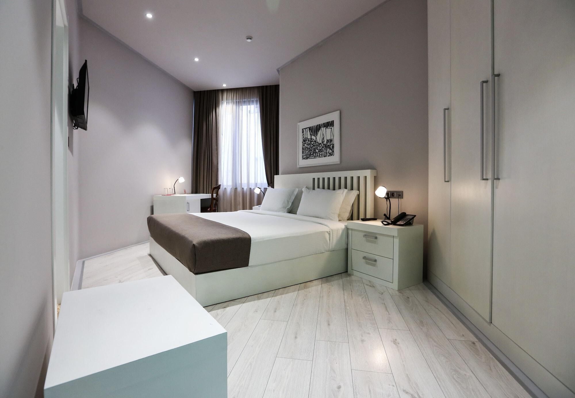 A modern hotel room with a bed, bedside tables, a wardrobe, and a television.