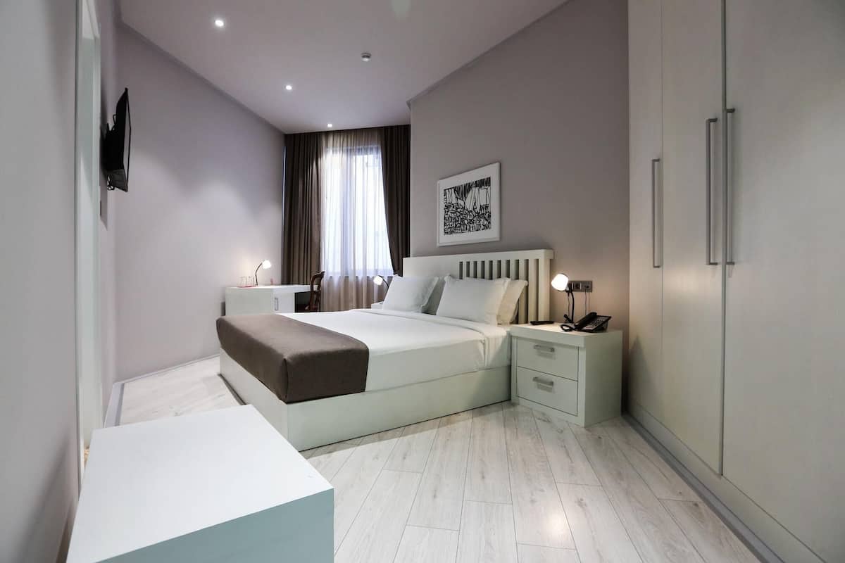 A modern hotel room with a bed, bedside tables, a wardrobe, and a television.