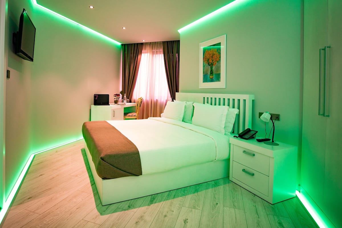 A modern hotel room with a large bed, bedside tables, a desk, and a TV mounted on the wall.
