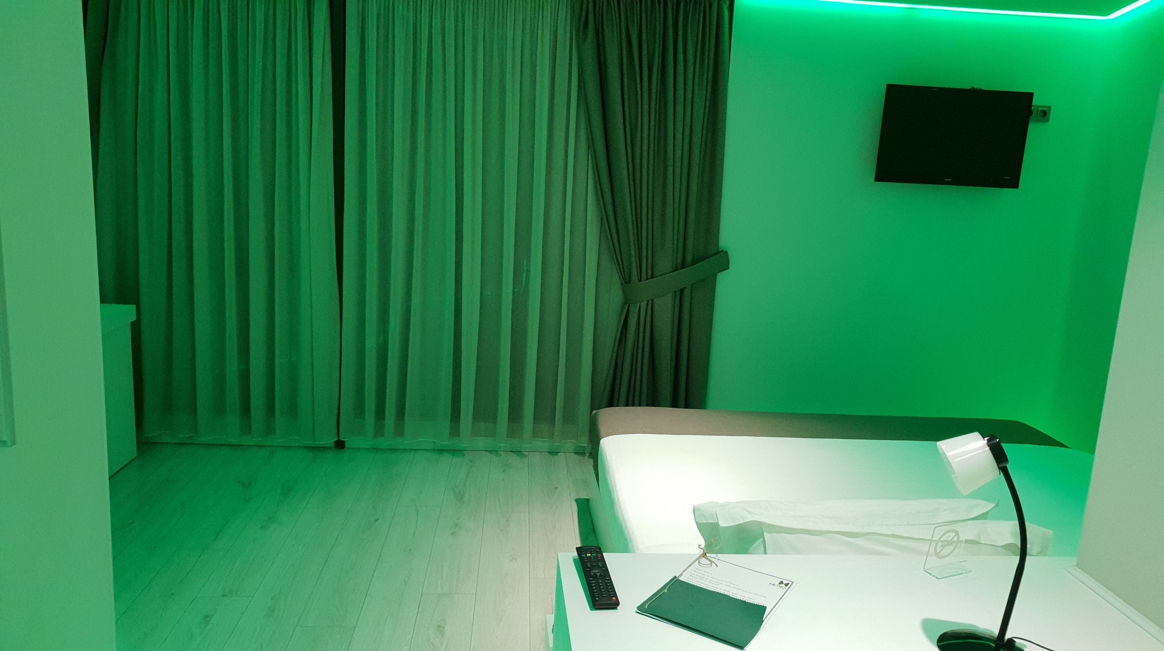 A hotel room with a bed, a desk with a lamp, a remote control, and a notebook.