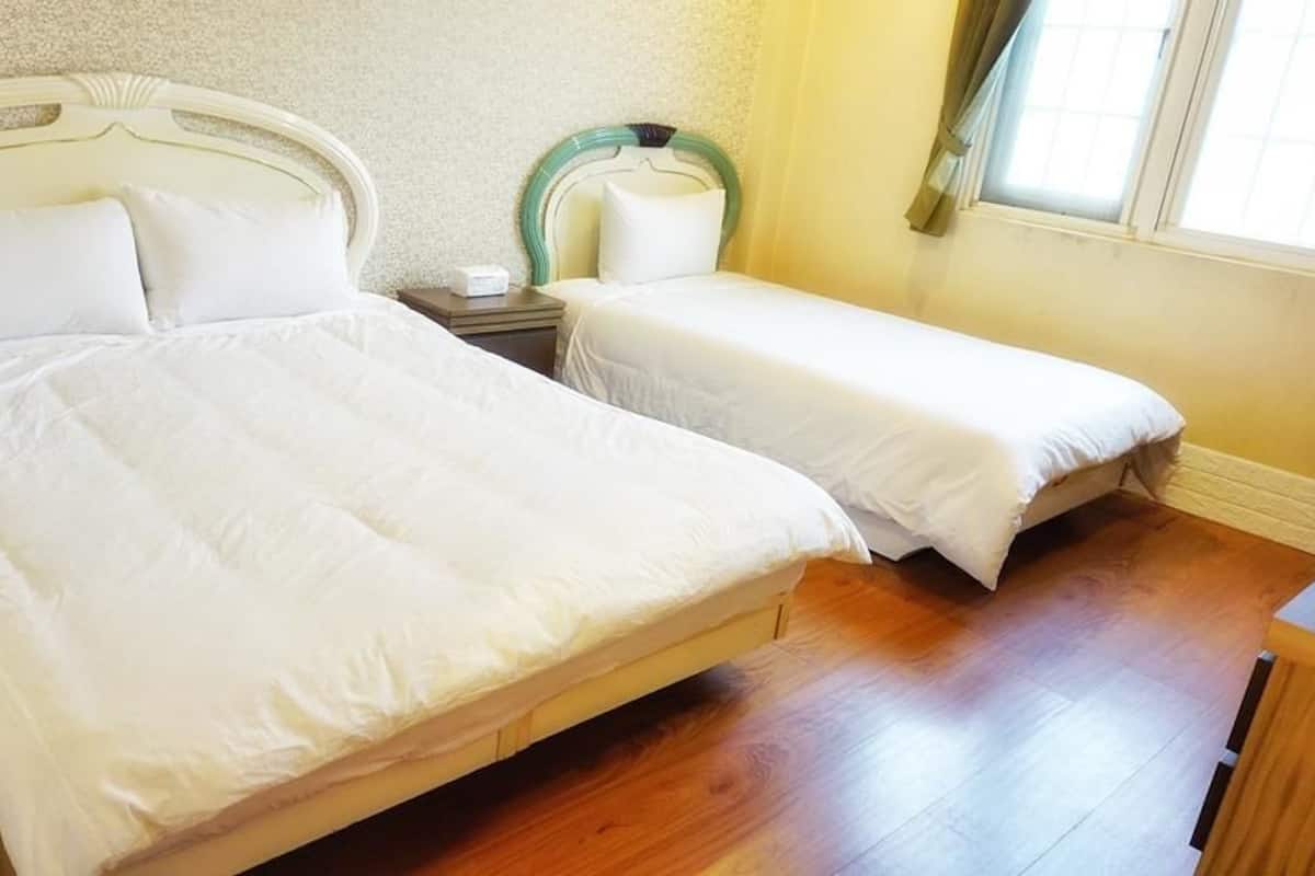 A double bed with a wooden frame and white bedding, a bedside table with a lamp, and a window with curtains.