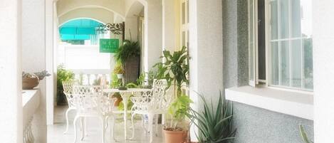 A covered outdoor area with a table and chairs, potted plants, and a window.