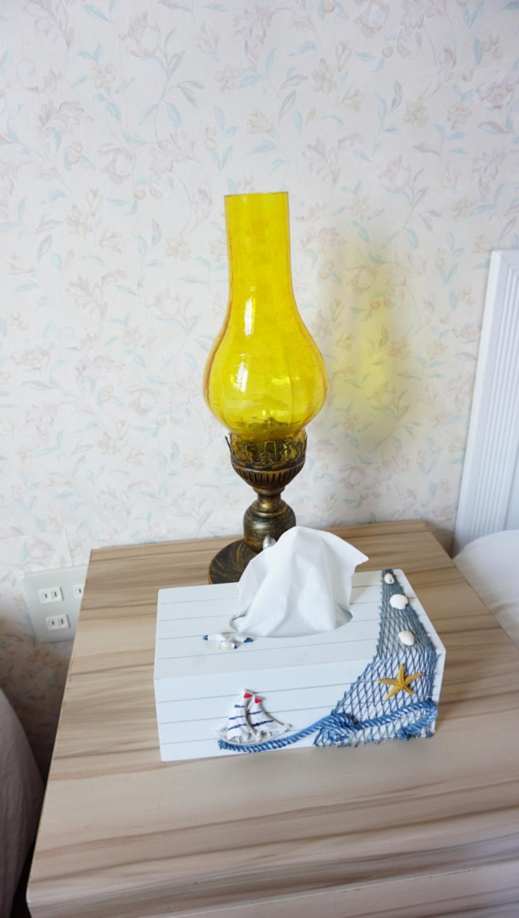 A bedside table with a yellow lamp, a tissue box, and a decorative item.