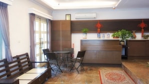 Een moderne woonkamer met een bank, eettafel en stoelen. Er is een keuken met een aanrecht en kasten. Sierplanten en rode lantaarns zijn zichtbaar.