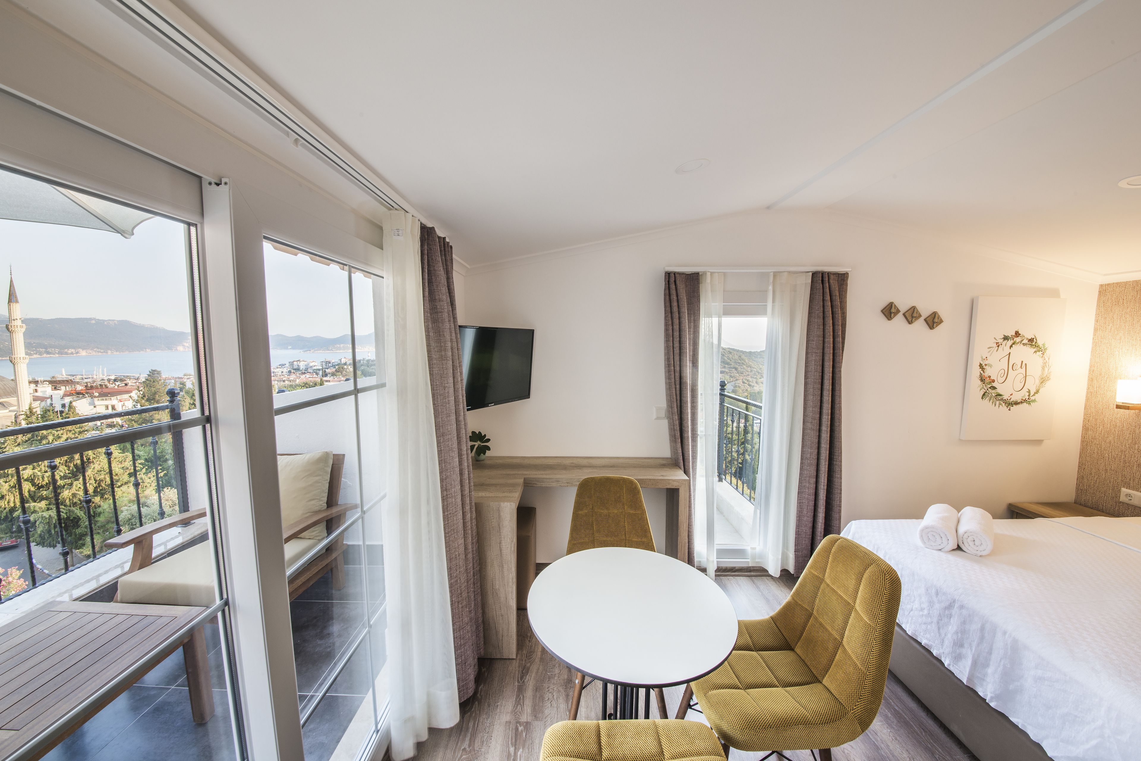 A hotel room with a balcony, a bed, a TV, a small table, and a sofa.