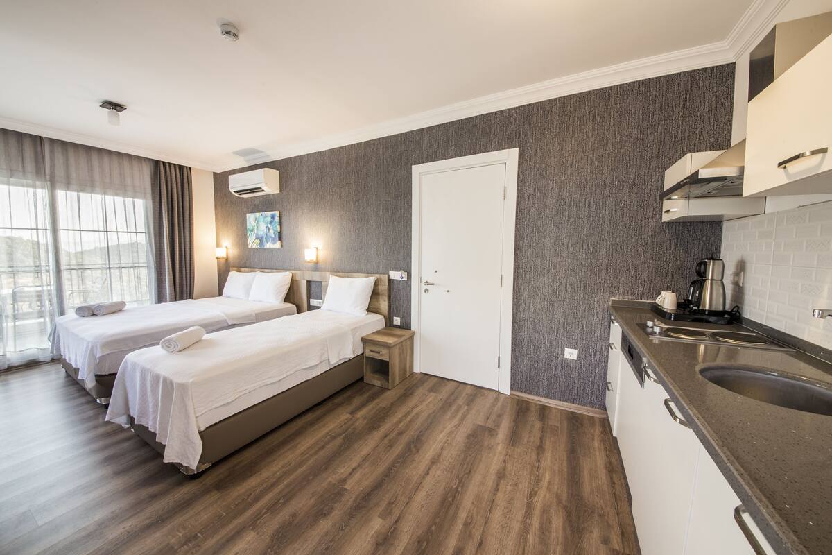 A hotel room with two beds, a kitchenette, and a bathroom.