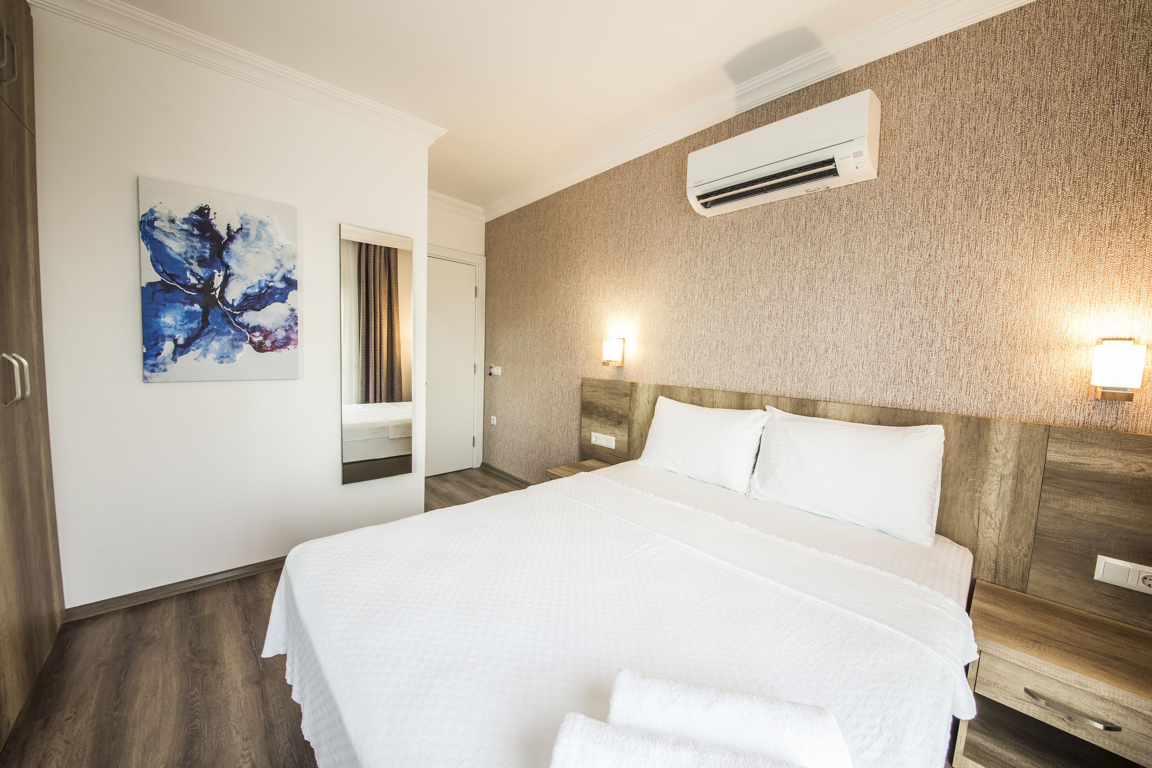 A hotel room with a large bed, a wall-mounted air conditioner, and a painting on the wall.