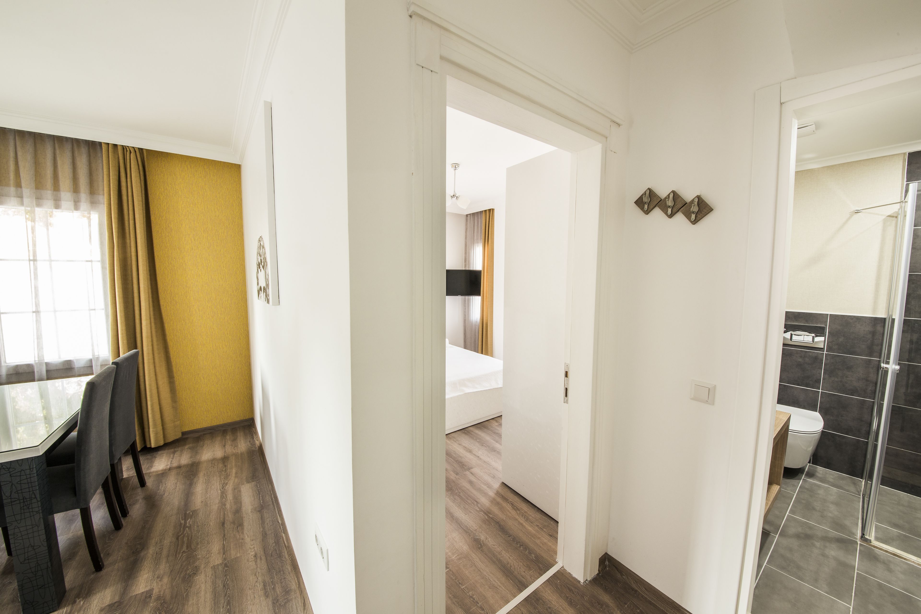 A hotel room with a wooden floor, a dining area with a table and chairs, a bathroom with a shower, and a bedroom with a bed.