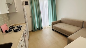 Una cocina moderna con armarios blancos, una estufa a gas y una encimera. En la sala de estar, hay un sofá beige y una mesa blanca.