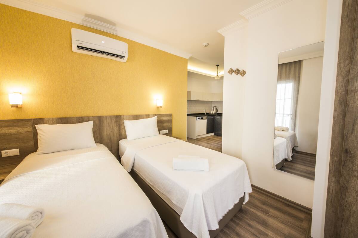 A hotel room with two beds, a kitchenette, and a mirror reflecting the room.