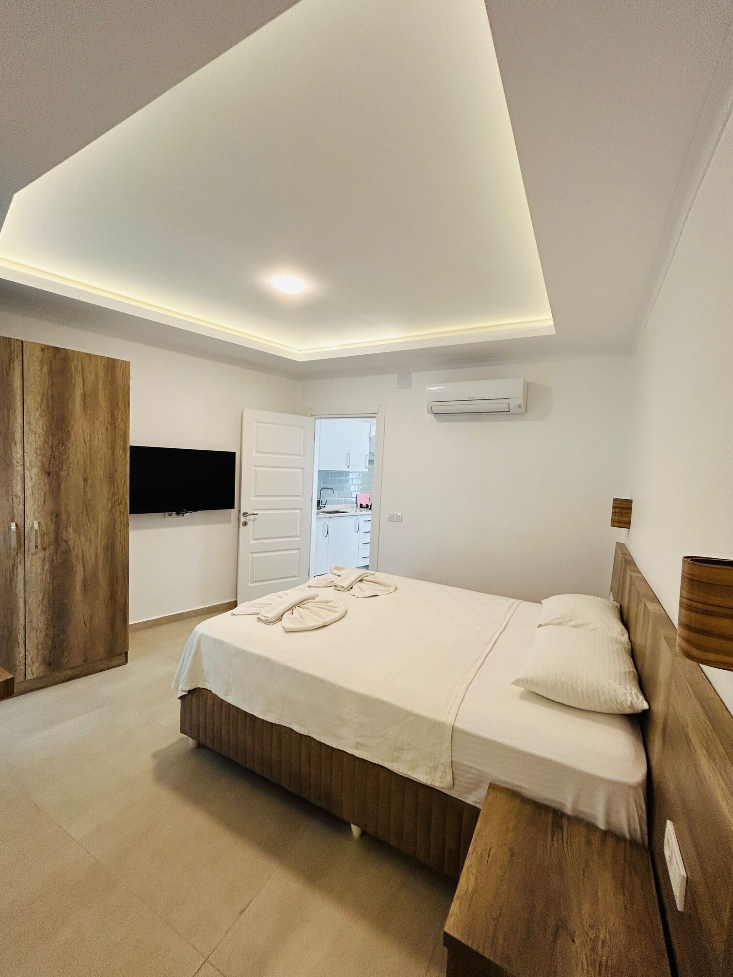 Une chambre à coucher moderne avec un grand lit, une armoire en bois et une vue sur la cuisine grâce à une porte ouverte.