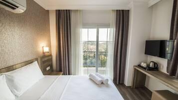 Habitación de hotel con cama, televisor, escritorio con tetera y ventana con cortinas.