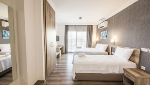 Habitación de hotel moderna con dos camas, un espejo grande, suelo de madera y vista a la ciudad por la ventana.