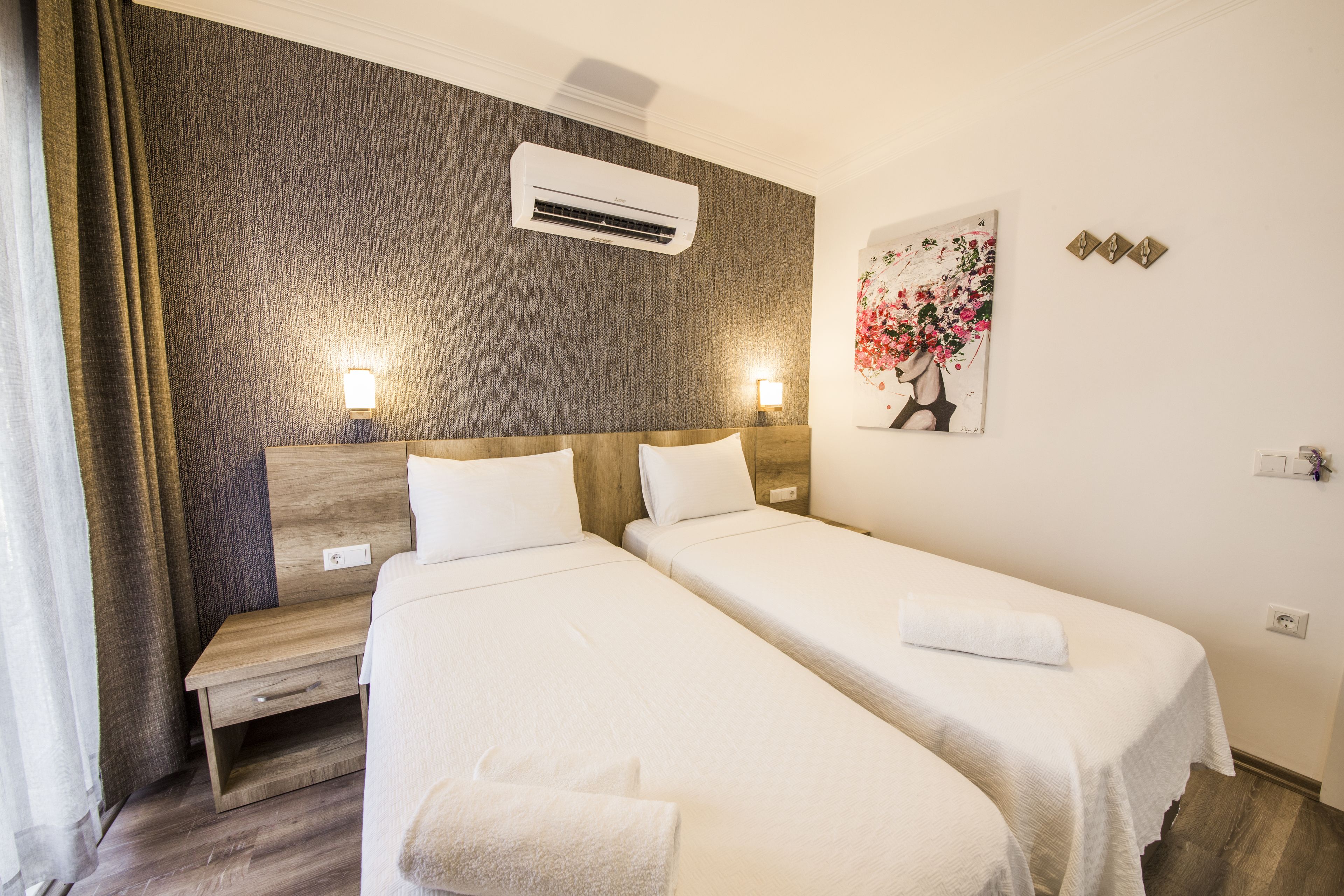 Ein Hotelzimmer mit zwei Betten, einem Holz-Kopfteil, einer Klimaanlage, einem Nachttisch und einer Wandleuchte.