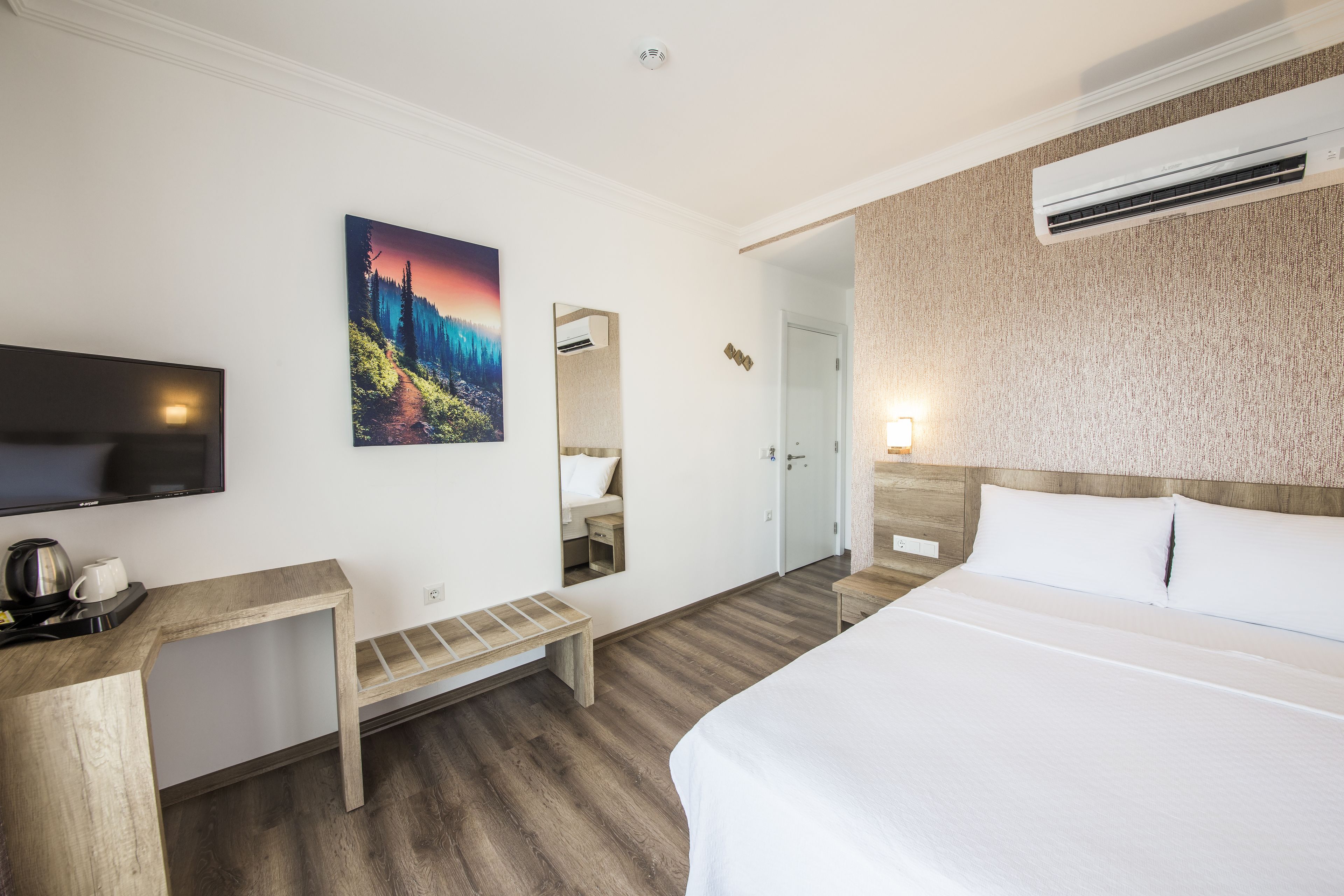 Een hotelkamer met een bed, een televisie, een bureau, een bankje en een schilderij aan de muur.