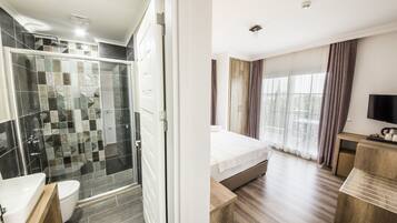 A modern hotel room with a shower, toilet, and a bed with a TV.