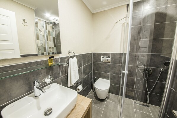 A modern bathroom with a glass shower enclosure, a white sink, and a toilet. - Dekatria Rooms & Aparts (Kas)