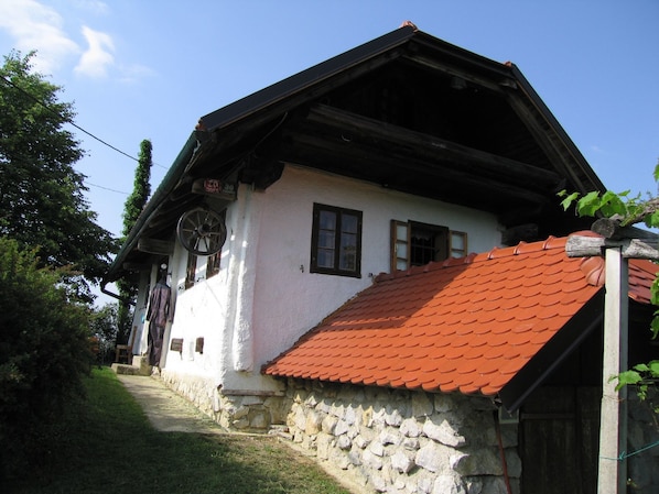 A traditional stone house with a red-tiled roof, a wooden staircase leading to the entrance, and a clear blue sky.