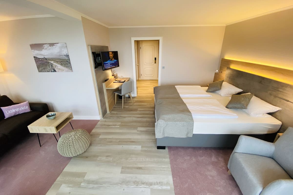 A modern hotel room with a bed, a sofa, a desk, and a TV.