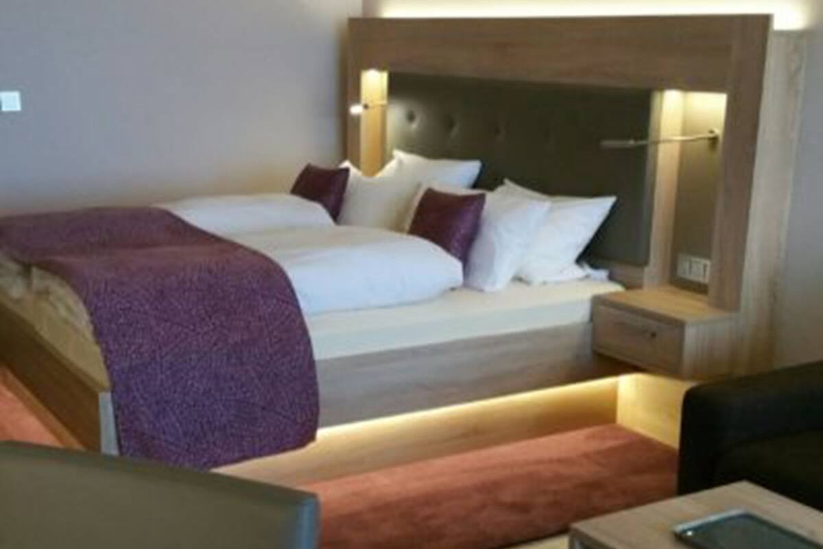 A modern hotel room with a large bed, bedside tables, a chair, and a small desk.