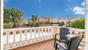Un balcone con ringhiera bianca, due sedie nere e un tavolo di legno.