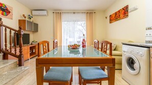 Zona pranzo con tavolo in vetro, sedie in legno, televisore e lavatrice sullo sfondo.