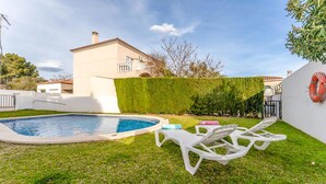 Una piscina con una piccola vasca idromassaggio, circondata da un prato curato e un edificio bianco con balconi.