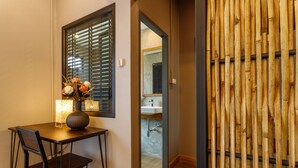 A room with a wooden table, a chair, a vase with flowers, a window with blinds, and a bamboo wall. - Hostel One Art & Gallery (Chiang Mai)