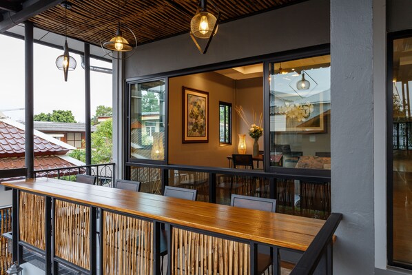 Un restaurante con mesa y sillas de madera, ventanas amplias y luces colgantes.