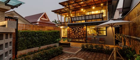 A two-story house with a covered patio, a stone well, and a wooden fence.