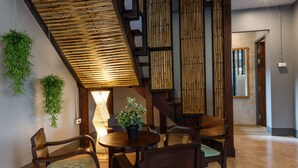 A wooden staircase with a bamboo railing, a round wooden table with chairs, and hanging plants. - Hostel One Art & Gallery (Chiang Mai)