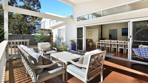 A modern outdoor patio with a dining area, white furniture, and a view of the backyard. - Calming Waters - Pet Friendly - Community Pool (Callala Beach)