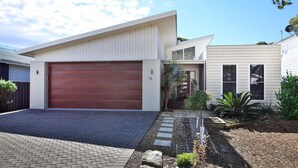 A modern two-story house with a large garage door, a small front porch, and a well-maintained garden. - Calming Waters - Pet Friendly - Community Pool (Callala Beach)