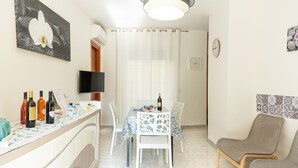Un coin repas avec une table dressée pour deux personnes, un téléviseur fixé au mur et une horloge au mur.