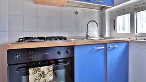 Une cuisine équipée d’une cuisinière à gaz, d’un four, de placards bleus et d’une fenêtre.
