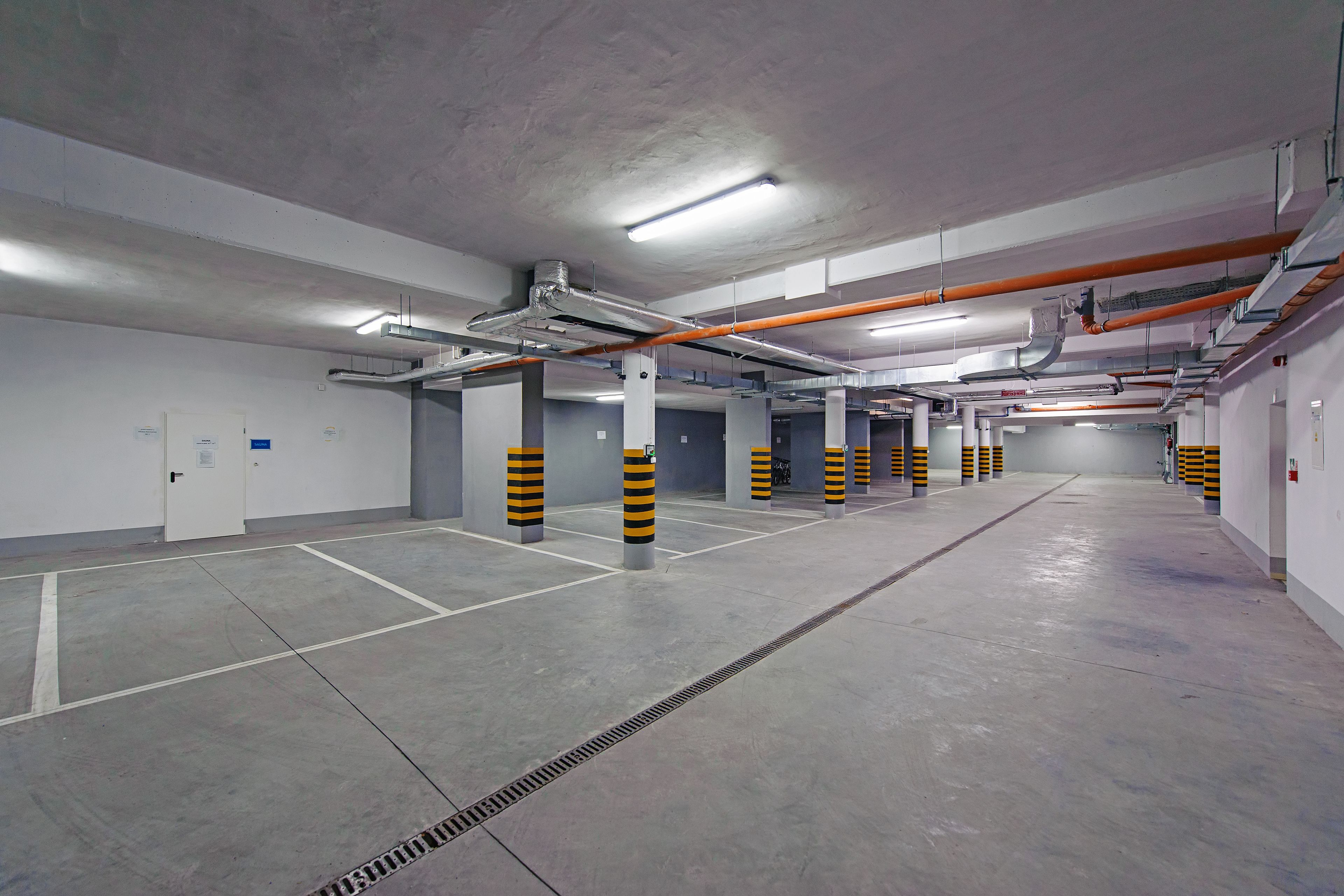 A clean, empty parking garage with concrete floors, white walls, and orange and black striped pillars.