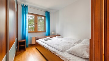 A bedroom with a bed, a window with curtains, a bedside table, and a lamp.