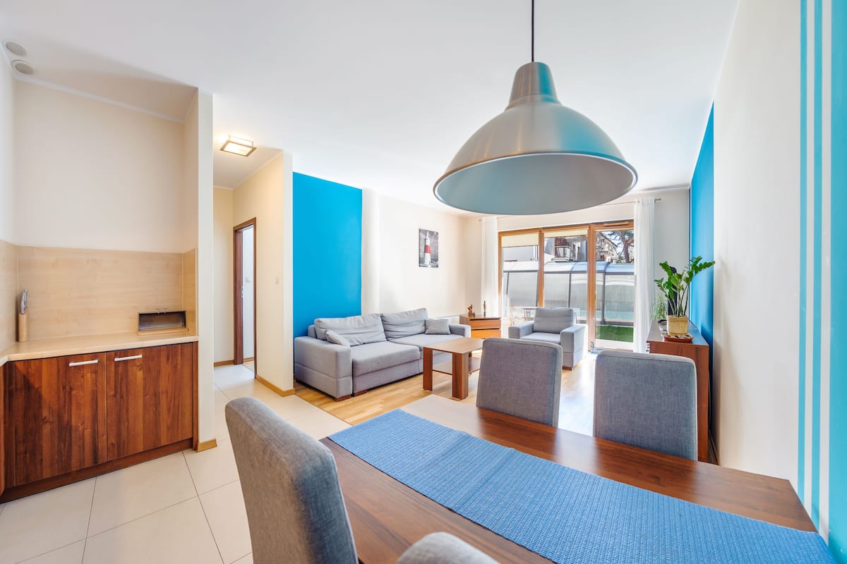 A modern living room with a wooden dining table, grey sofas, and a large pendant light.